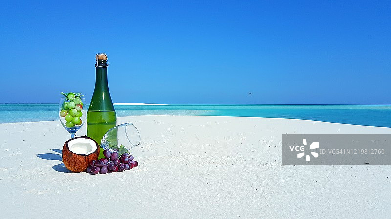 异国情调海滩的白色沙滩上，带有葡萄和玻璃杯的香槟酒瓶图片素材