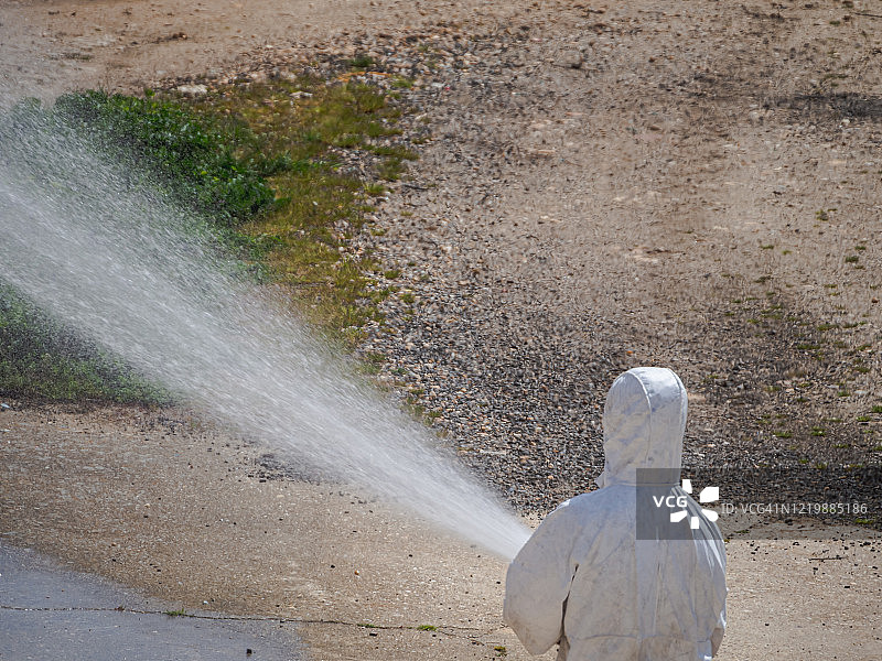 疫情期间身穿防护装备、用水管喷洒的人图片素材