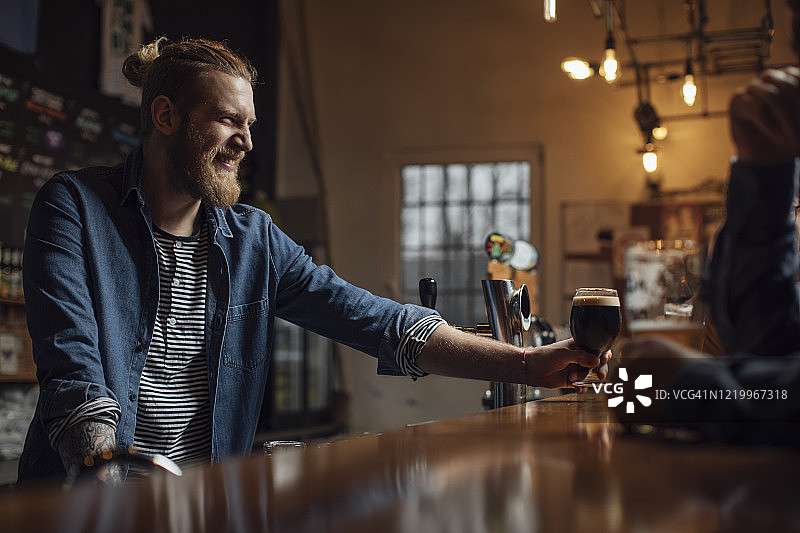 金发时髦酒保在吧台为顾客提供啤酒图片素材