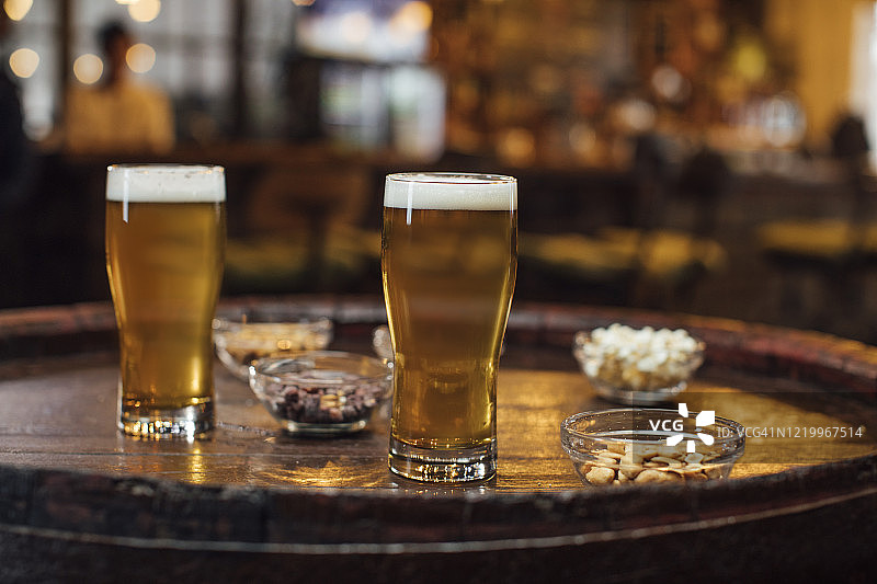 当地酒吧欢乐时光：两杯淡啤酒和木桌上的小吃图片素材
