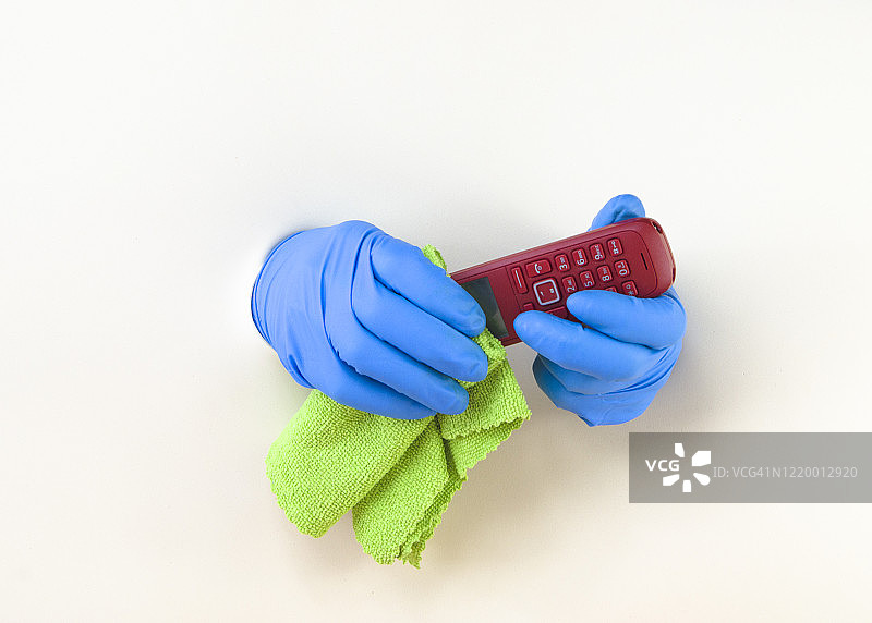 男人戴橡胶手套擦拭消毒电话，预防新型冠状病毒（COVID-19）图片素材