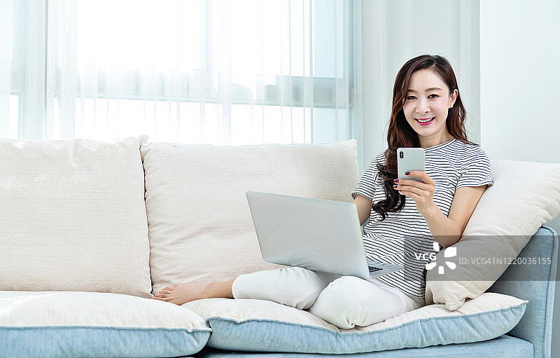 坐在沙发上使用手机和笔记本电脑的漂亮女人图片素材