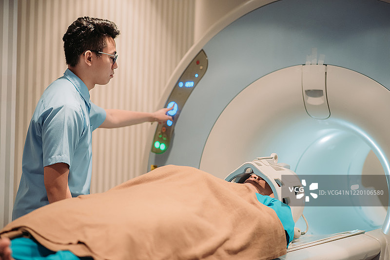中国男护士帮助成年男性患者在医院进行MRI扫描图片素材