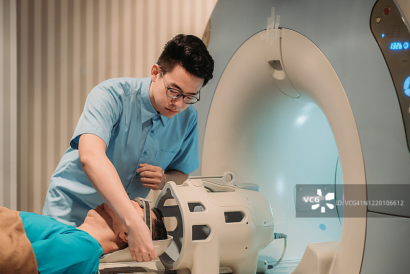 亚裔男护士在医院核磁共振扫描前为成年男病人调整头套图片素材