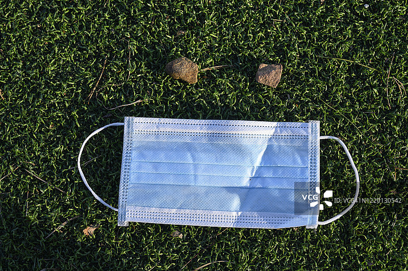 绿色人造草地上，用两块石头组成面部的防护口罩图片素材