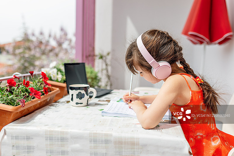 戴着耳机用笔记本电脑做作业的小女孩图片素材