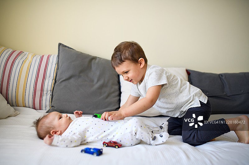 在家中，小男孩和他的小妹妹在床上玩汽车图片素材