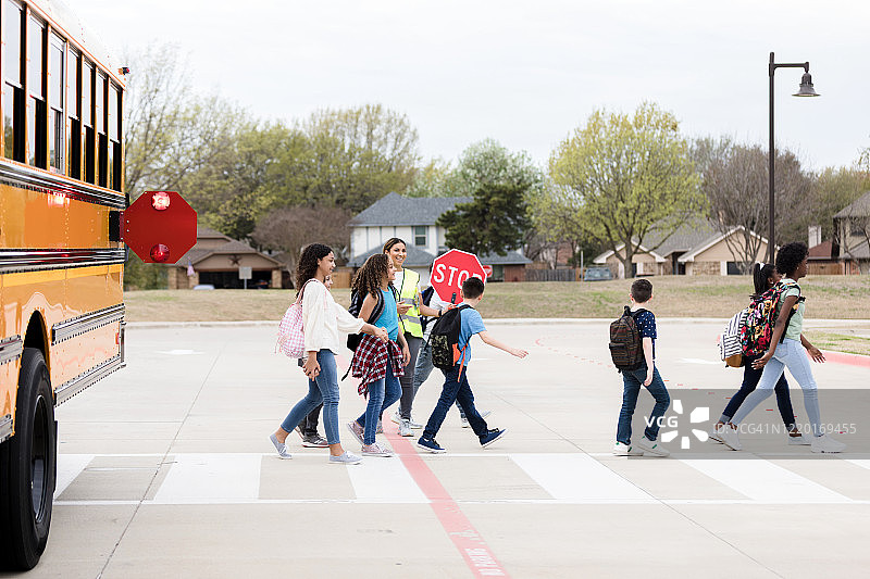 交通管理员举着停止标志，孩子们走过人行横道图片素材
