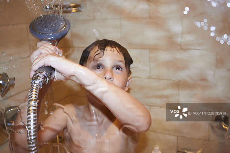 在淋浴房里的小男孩，他站在玻璃后面，把水喷在玻璃上。图片素材