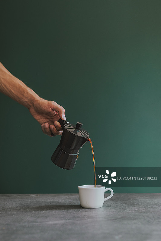 手持摩卡壶将新鲜浓缩咖啡倒入白色杯子图片素材