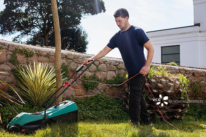 年轻男人在花园里割草图片素材