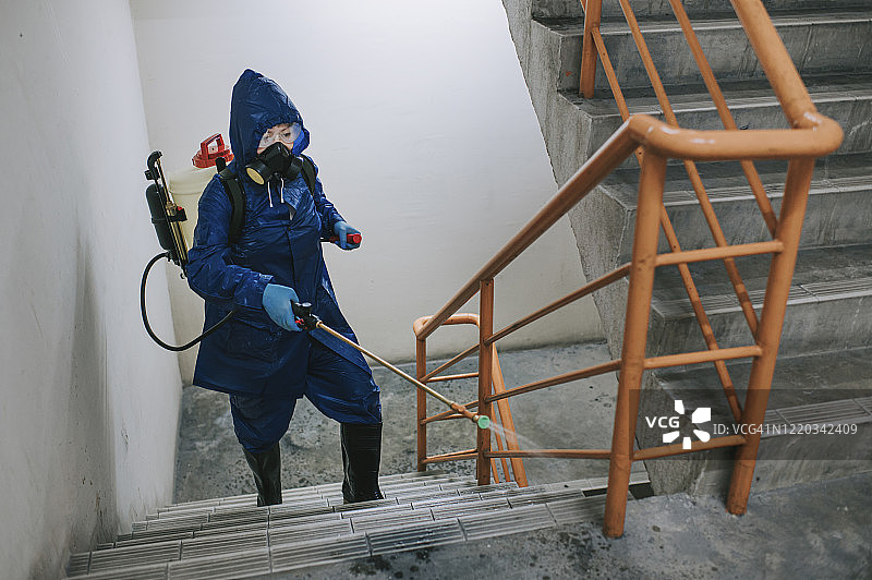 一位身穿防护服的女人在楼梯上喷洒消毒图片素材