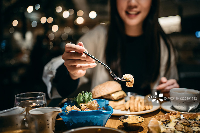 微笑的年轻女子在餐厅里享受美食并分享食物图片素材