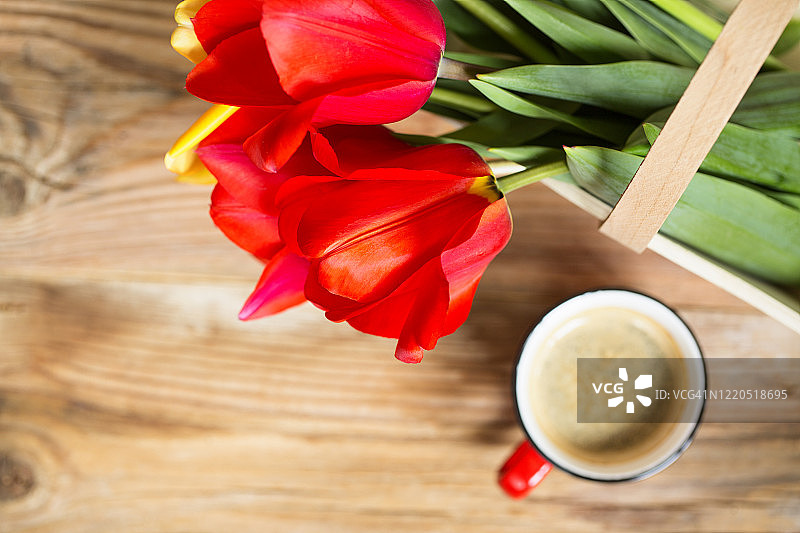 木篮中的红色和黄色郁金香，木制背景上的红咖啡杯俯视图。留白。焦点在郁金香上图片素材