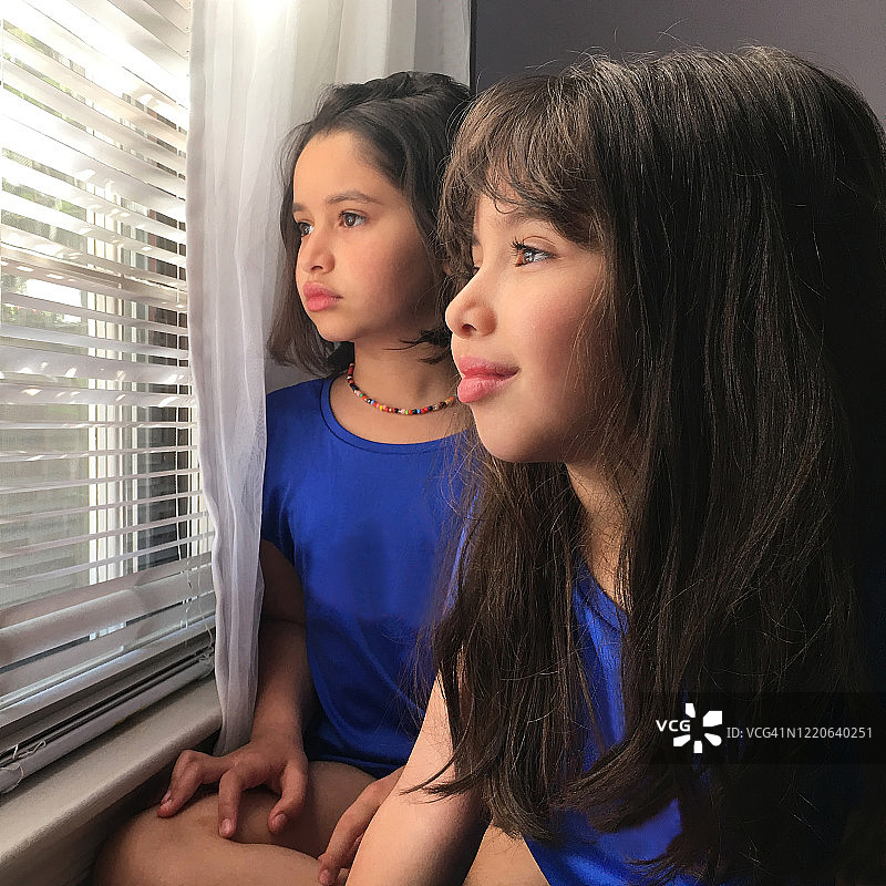 新冠疫情封锁期间，姐妹俩透过百叶窗向外看图片素材