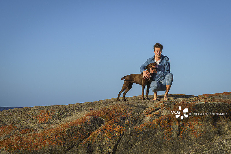 青年男子在海滩岩石边与拉布拉多犬互动图片素材