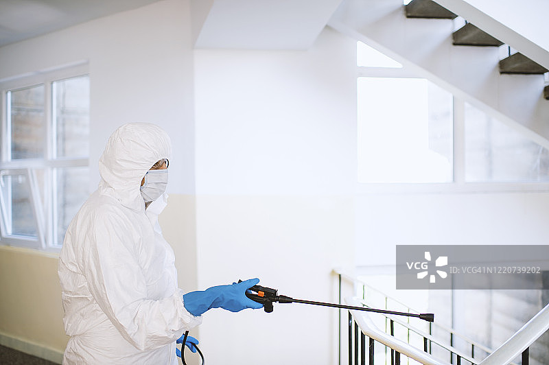 身穿白色化学防护服消毒建筑物走廊和台阶的男人图片素材