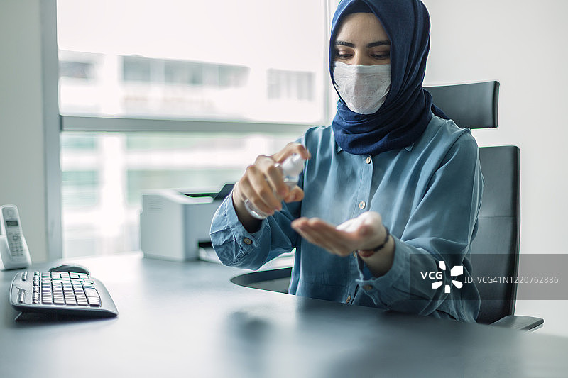 戴着头巾的年轻女人用洗手液消毒她的手图片素材