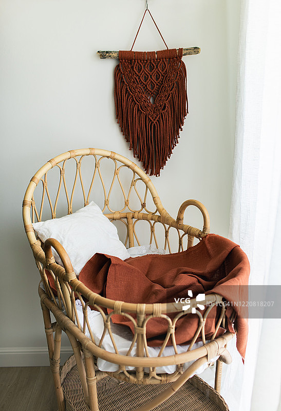 时尚斯堪的纳维亚风格新生儿婴儿房，配天然藤条摇篮。现代内饰，白色背景墙，木制家具和手工棉制棕色macrame挂毯。图片素材