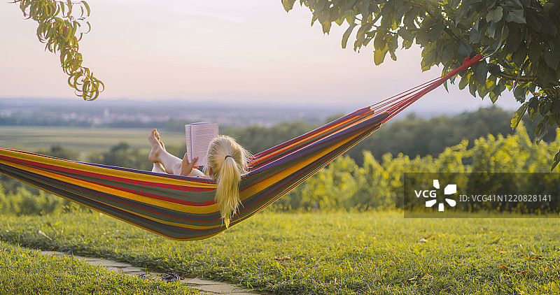 在日落时分在吊床上看书的女人图片素材