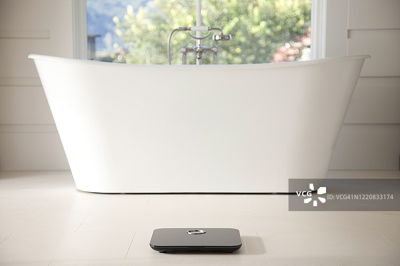 白色大理石地板上带浴缸的黑色数字浴室秤图片素材