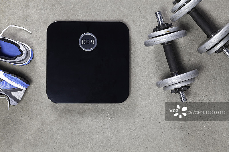 灰色水泥地面上的黑色电子秤、运动鞋和哑铃图片素材
