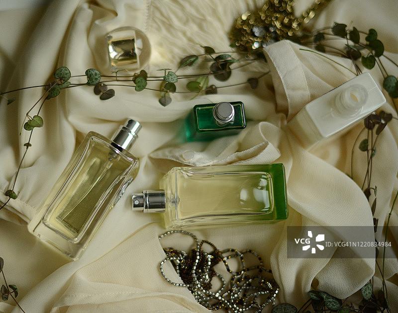 白色丝绸衬衫上的三瓶香水和一条项链图片素材