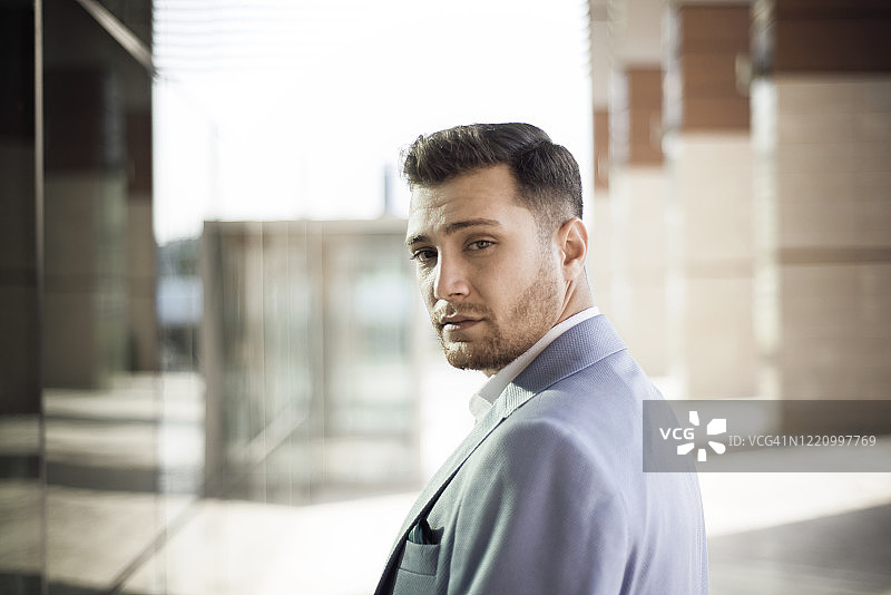 年轻商人回头看镜头，背景为办公楼图片素材