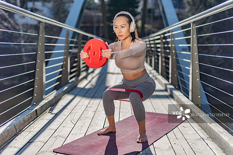 在阳光明媚的日子里在桥上做深蹲的年轻女子图片素材