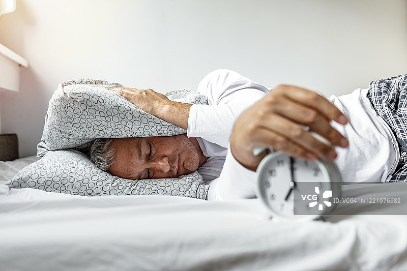 清晨在床上被闹钟吵醒的熟睡中年男人图片素材