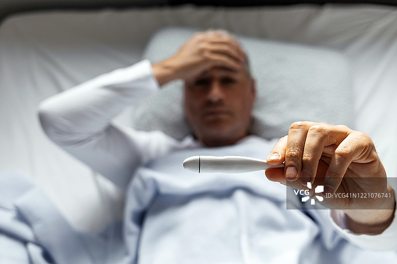 生病的男人用数字温度计测量体温图片素材