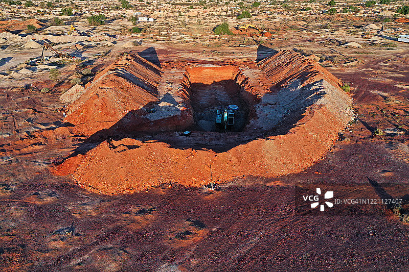 阳光照耀下的红色泥土墙，蛋白石矿尾矿形成的火山口状结构，以及澳大利亚内陆的推土机。图片素材