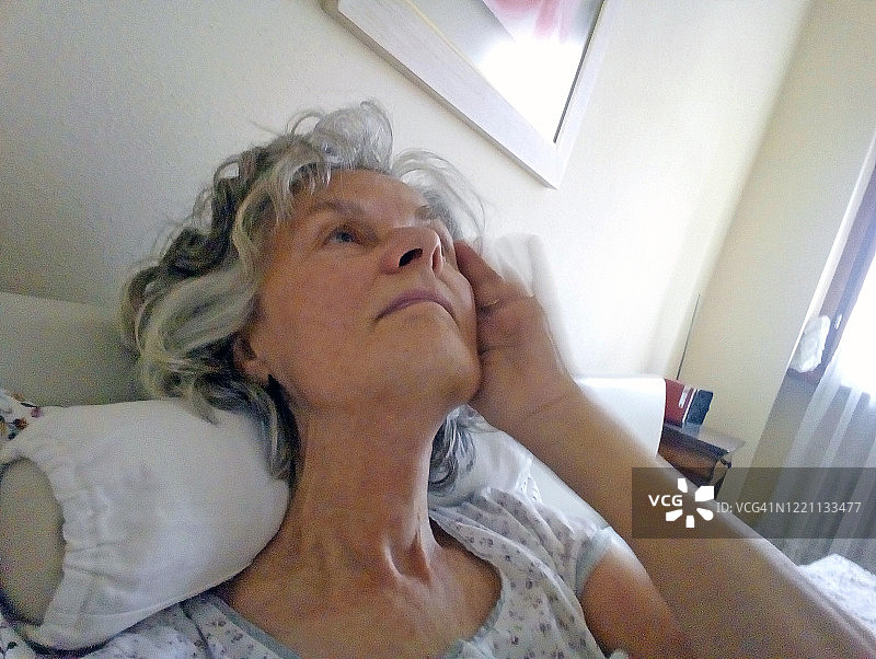 在床上，头部枕在靠垫上的年长女性图片素材