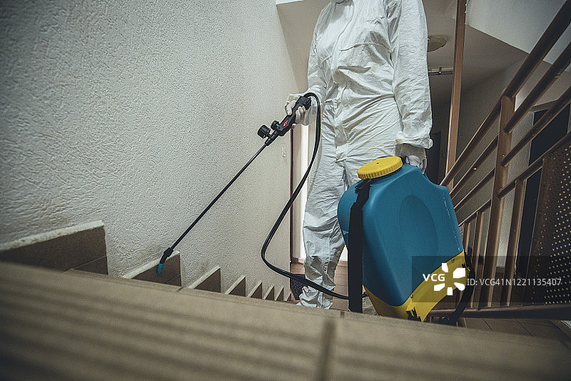 一名女子身穿防护服，对住宅楼空间进行消毒图片素材