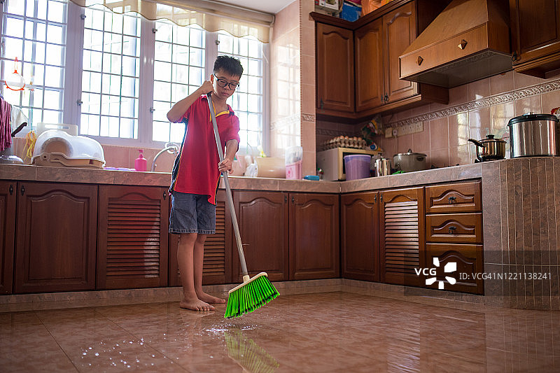 一名亚洲女人使用刮水器清洁厨房地板表面，因疫情居家隔离图片素材