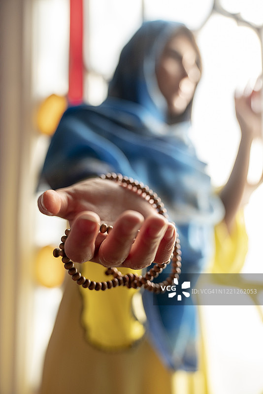 戴头巾的穆斯林妇女在清真寺祈祷，双手举起，手持念珠，宗教祈祷概念图片素材