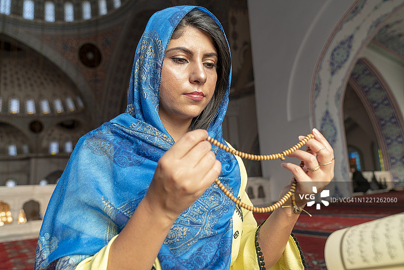 戴头巾的穆斯林妇女在清真寺祈祷，双手举起，手持念珠，宗教祈祷概念图片素材