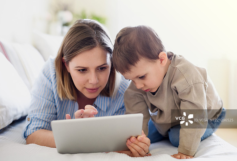 母亲和年幼的儿子在家中使用平板电脑的正面照图片素材