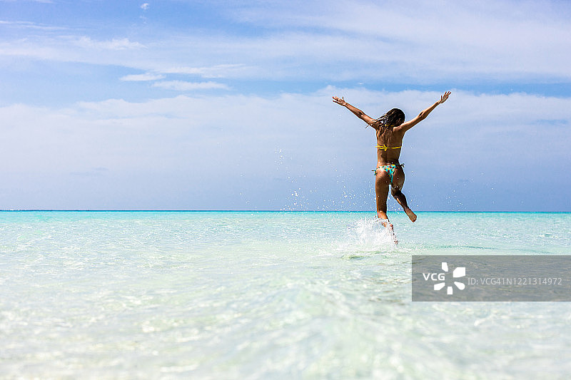 女子在夏日海边跳跃玩耍的背影图片素材