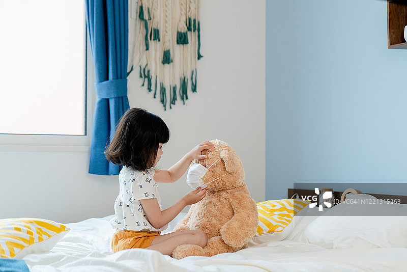 年轻女孩给她的泰迪熊戴上口罩图片素材
