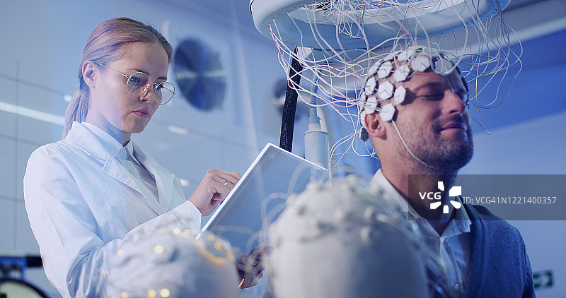 女科学家在实验室用脑电波扫描头盔检查男性大脑图片素材