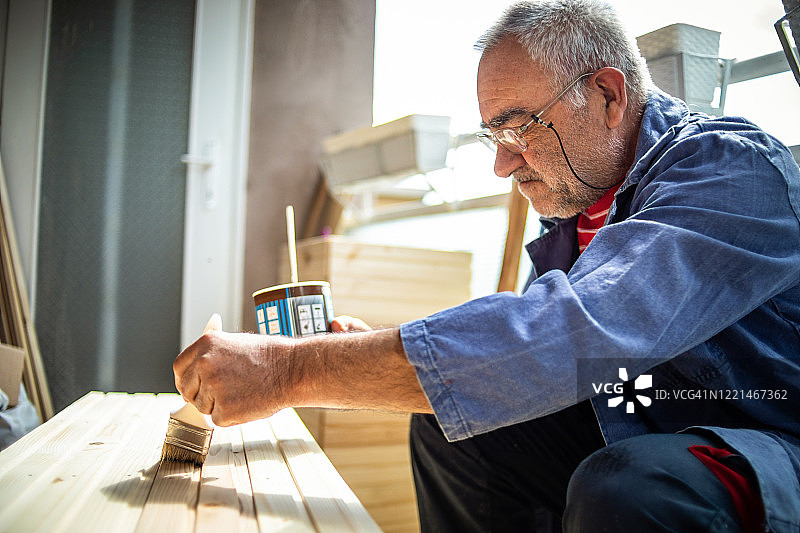 一位年长的男人在木质表面上涂油漆图片素材