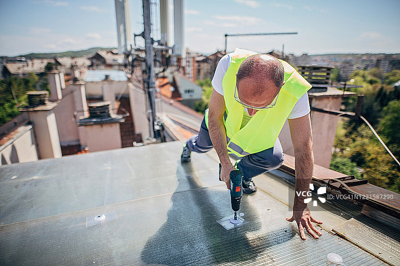 一位使用电动螺丝刀的中年屋顶维修工图片素材