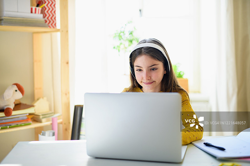 在家学习的女孩，戴着耳机用笔记本电脑图片素材