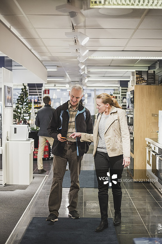 中年朋友站在电子商店里用智能手机交谈图片素材