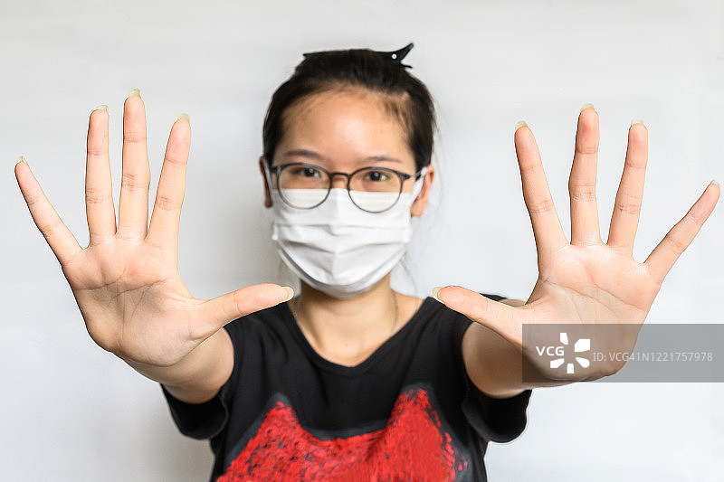 戴着外科口罩的女人为了保护病毒而做出停止手势以保持社交距离（焦点在她手上）图片素材