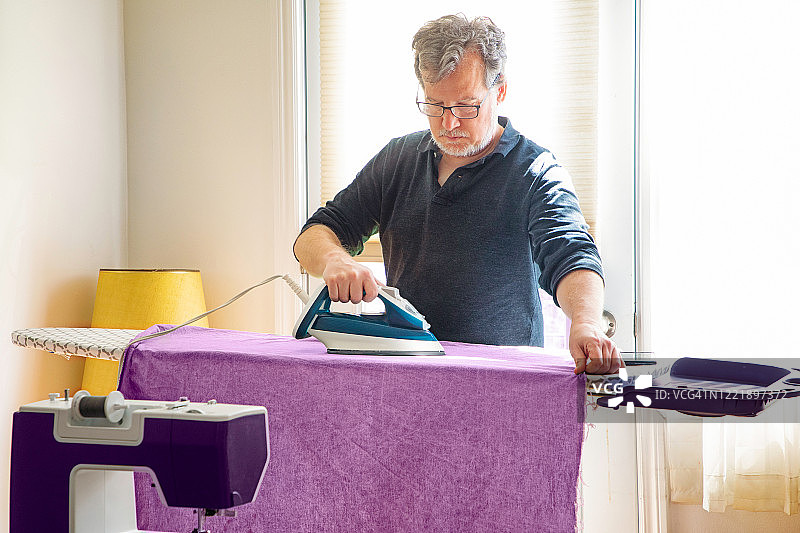 在客厅里熨烫紫色布料的老年男人图片素材