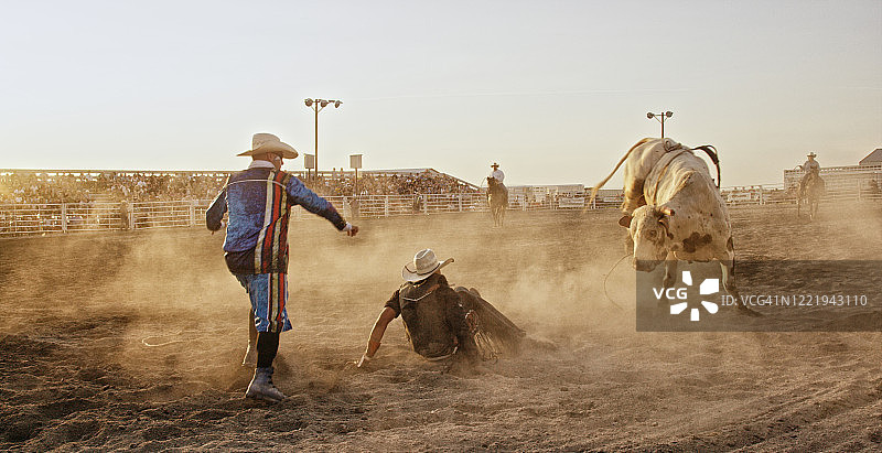 在日落时分，斗牛竞技场里，一个斗牛士从牛背上摔下来后，参加斗牛比赛，而小丑分散了牛的注意力图片素材