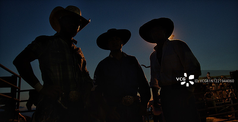 夜晚竞技斗牛活动中戴牛仔帽的三个人物剪影图片素材