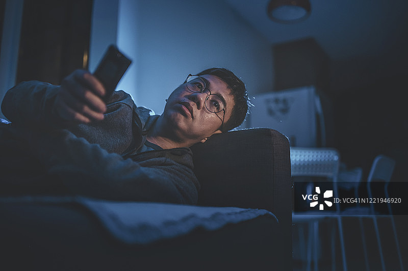 夜晚，中国男子独自在家靠在沙发上看电视图片素材